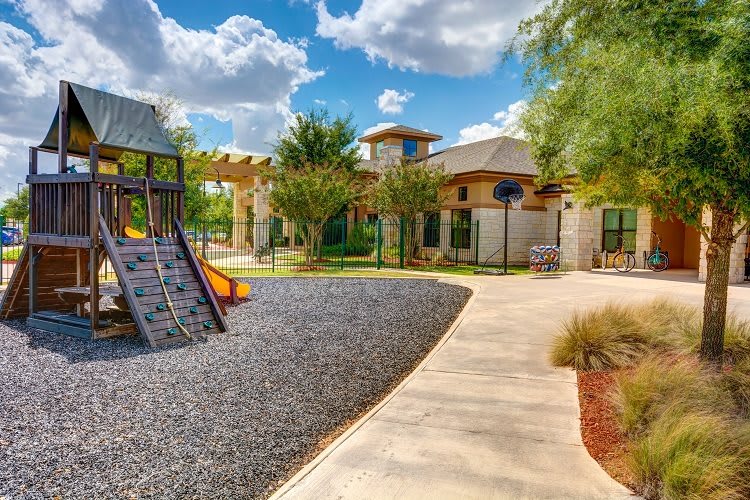 A sunny day at a children's playground with a nearby building and pathway.
