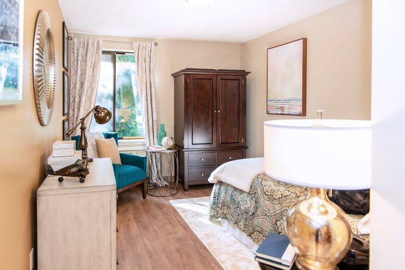 A cozy bedroom featuring a wooden wardrobe, decorative lamp, and an armchair by the window.