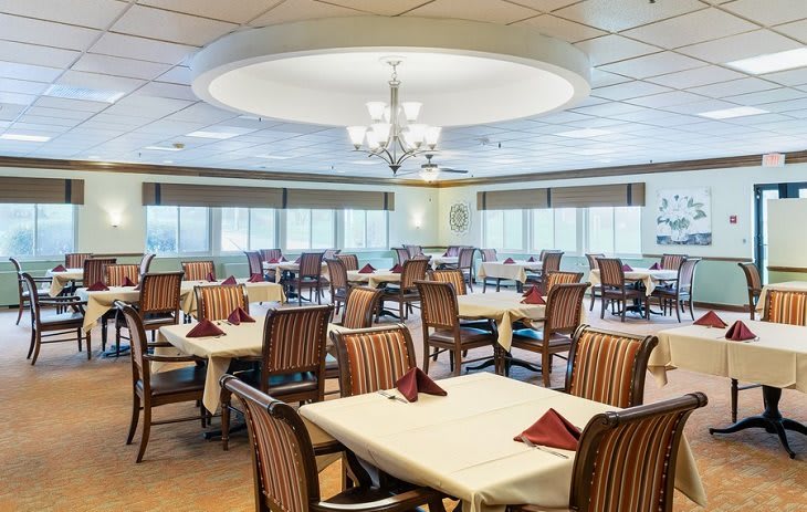 A spacious dining room with elegantly set tables and a central chandelier.