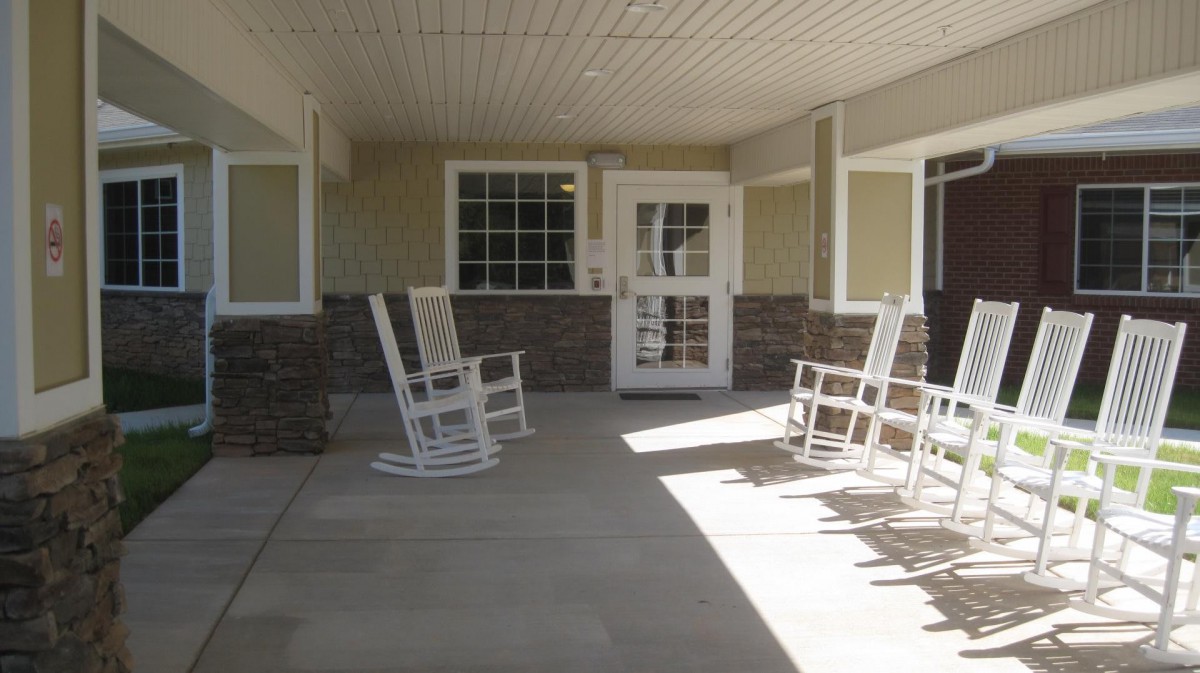 A covered porch with white rocking chairs and a glass door.