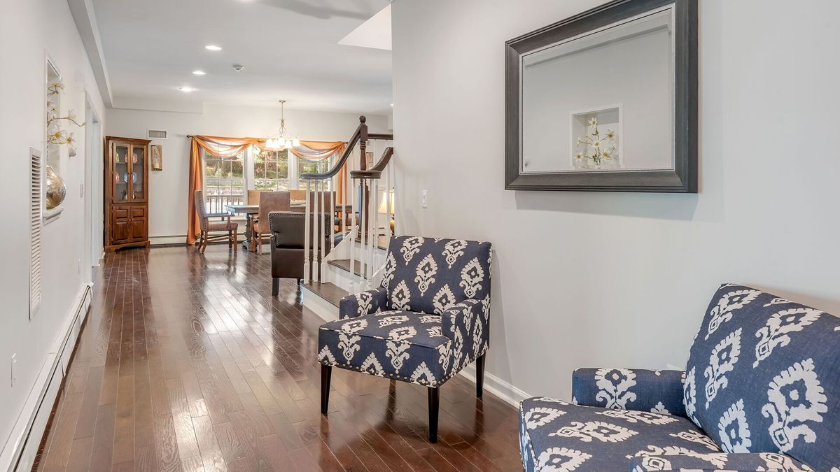 A cozy living area featuring patterned armchairs, a large mirror, and hardwood floors leading to an elegant dining space.