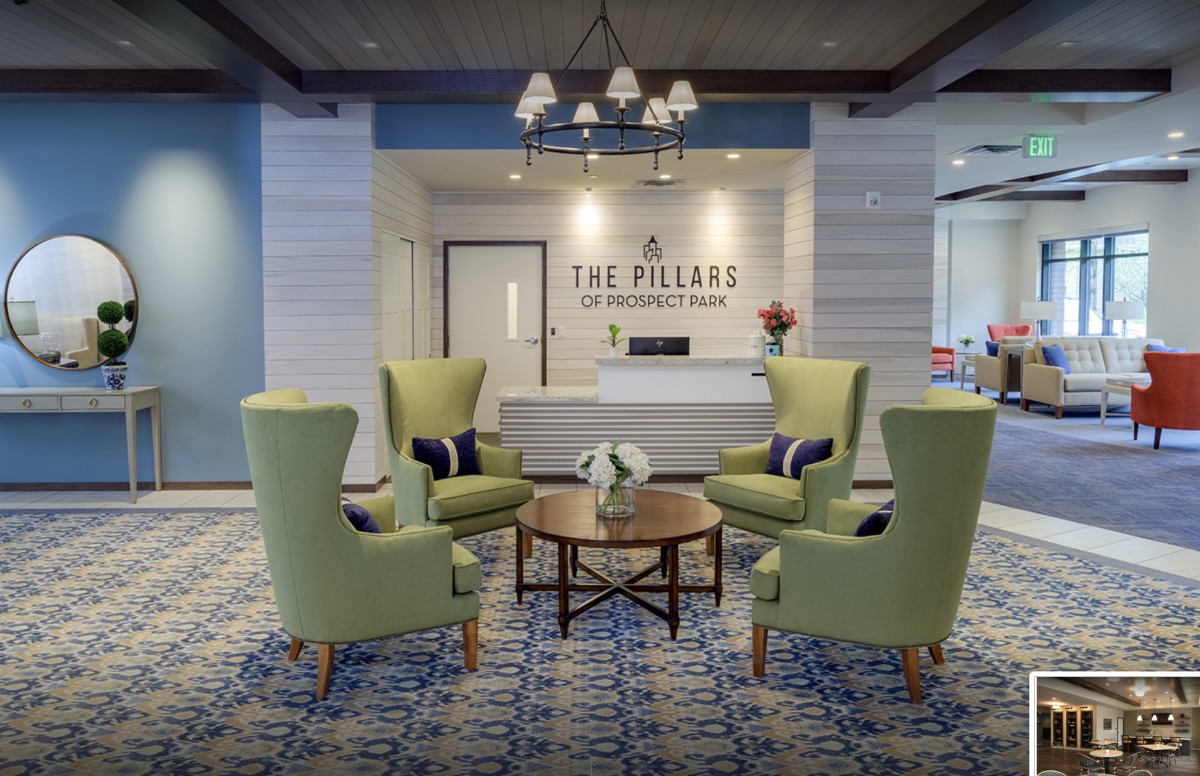 A modern lobby with green chairs, a central table, and a reception desk at The Pillars.