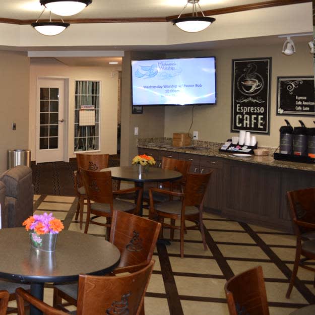 A cozy cafe interior with seating area, featuring tables and chairs, a menu board, coffee station, and decorative flowers.