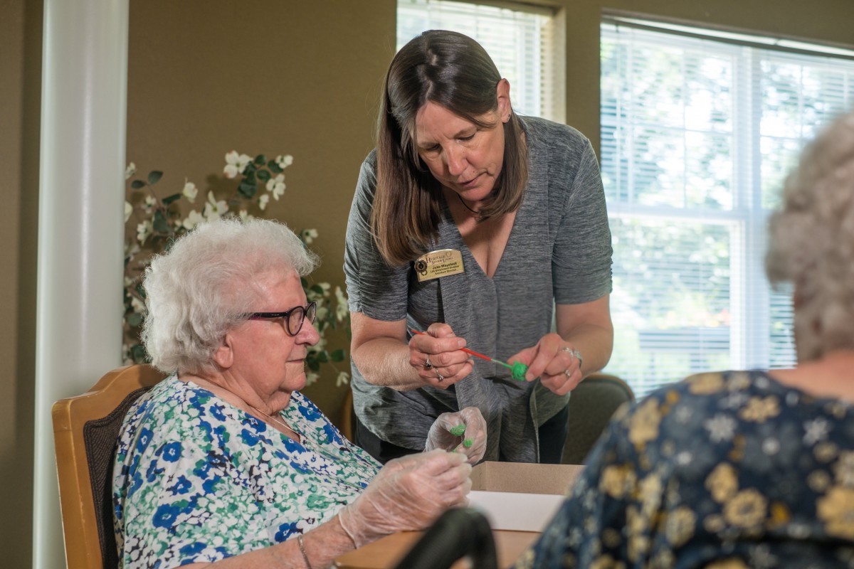 A caregiver assists an elderly person with an activity indoors.
