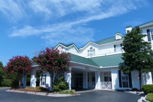 A sunny day view of a hotel with a green roof and surrounded by trees.