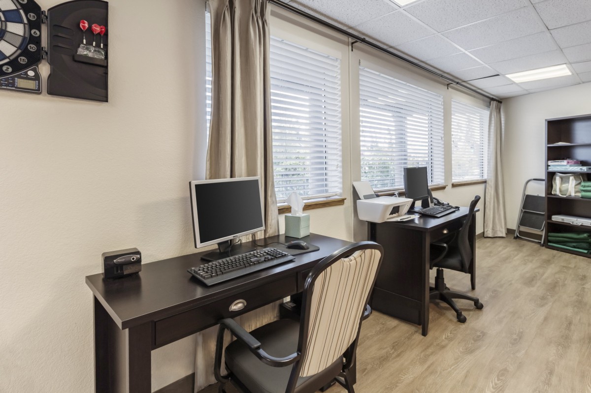 A modern office space featuring two desks with computers and chairs, situated near large windows with blinds.