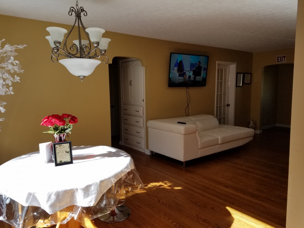 A cozy living room with a white sofa, wall-mounted TV, and a table with red flowers.