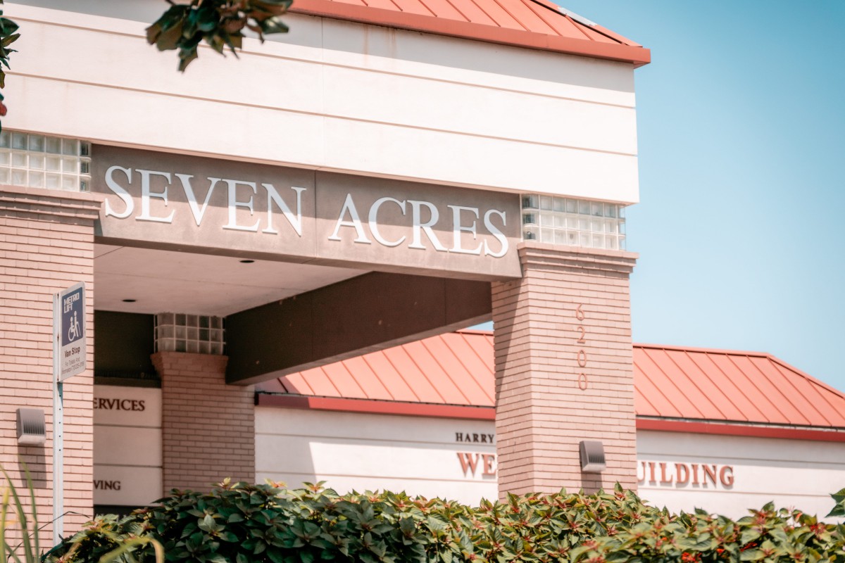 A sunny day view of a building with a red roof and signage reading 'SEVEN ACRES'.