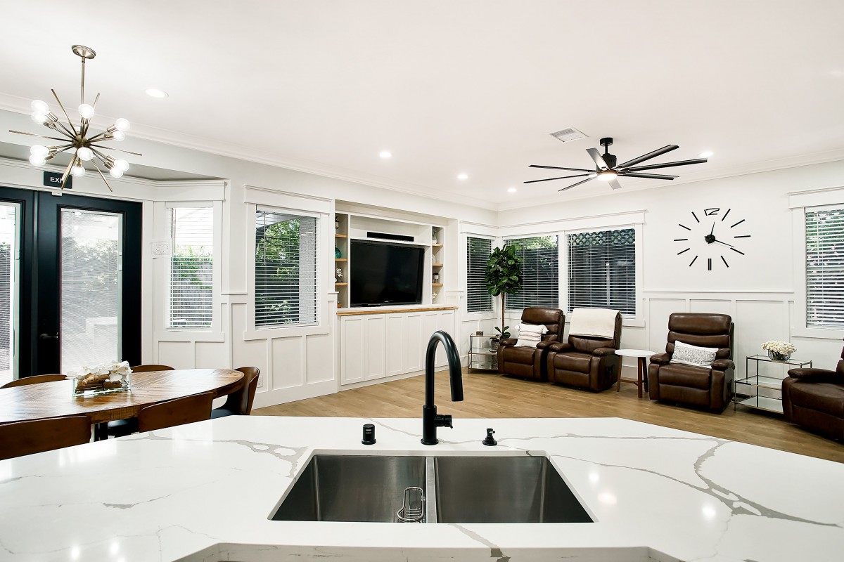 A modern open-concept living room with a view from the kitchen sink, featuring comfortable recliner chairs and a wall-mounted TV.