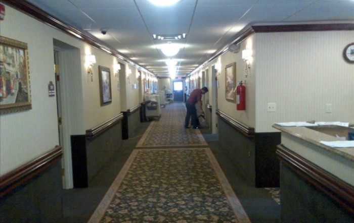 A hallway with carpeted floor and overhead lighting, featuring a person in the distance.