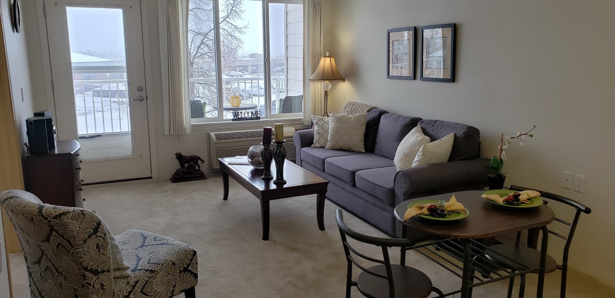 A cozy living room with a sofa, coffee table, and a large window letting in natural light.