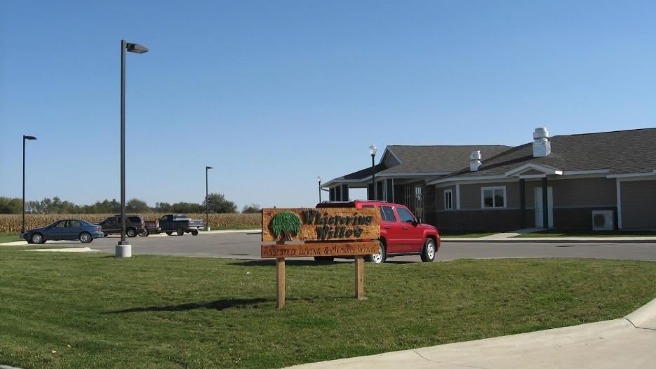 A suburban residential area with a house, red car, and a sign reading 'Silverado Village' under a clear blue sky.