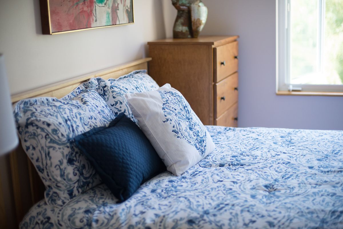 A cozy bedroom scene featuring a bed with blue floral bedding and accent pillows, alongside a wooden dresser.