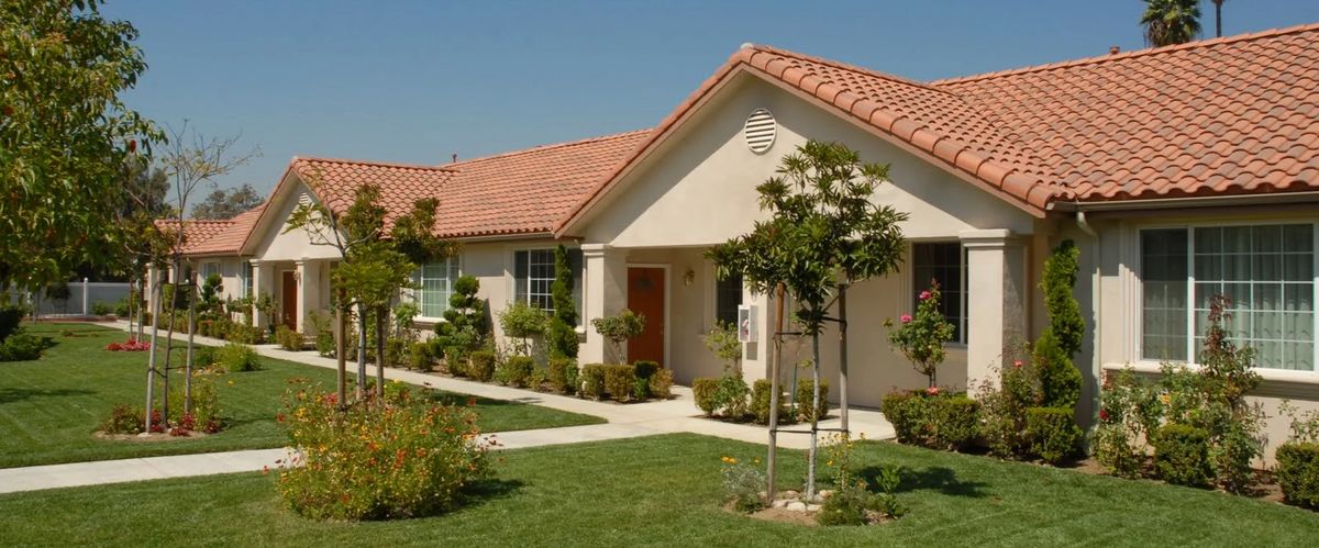 A well-maintained residential house with a tiled roof, surrounded by neat landscaping and a green lawn under a clear sky.