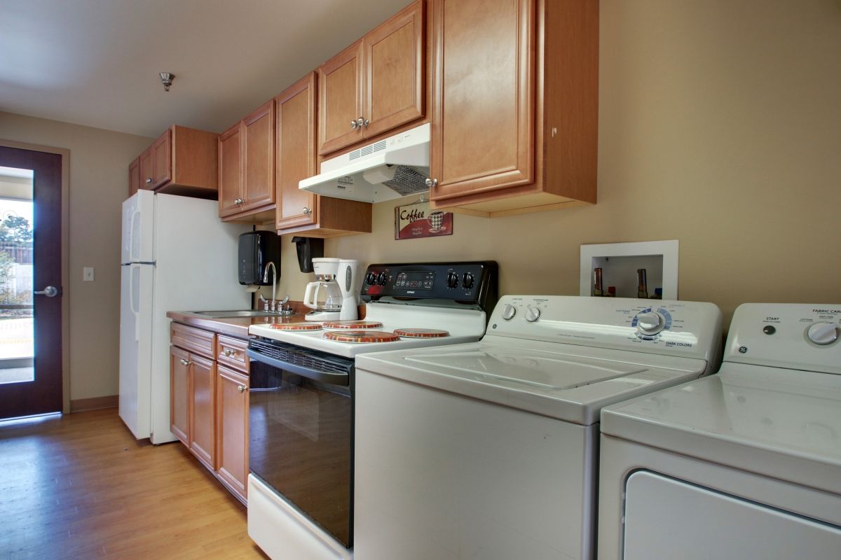 A kitchen with wooden cabinets, featuring appliances like a washer, dryer, and oven.