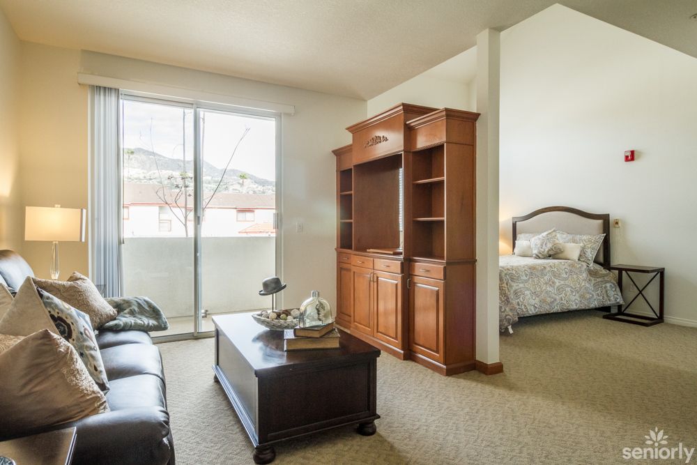 A cozy living room with a sofa, coffee table, and cabinet, opening into a bedroom.