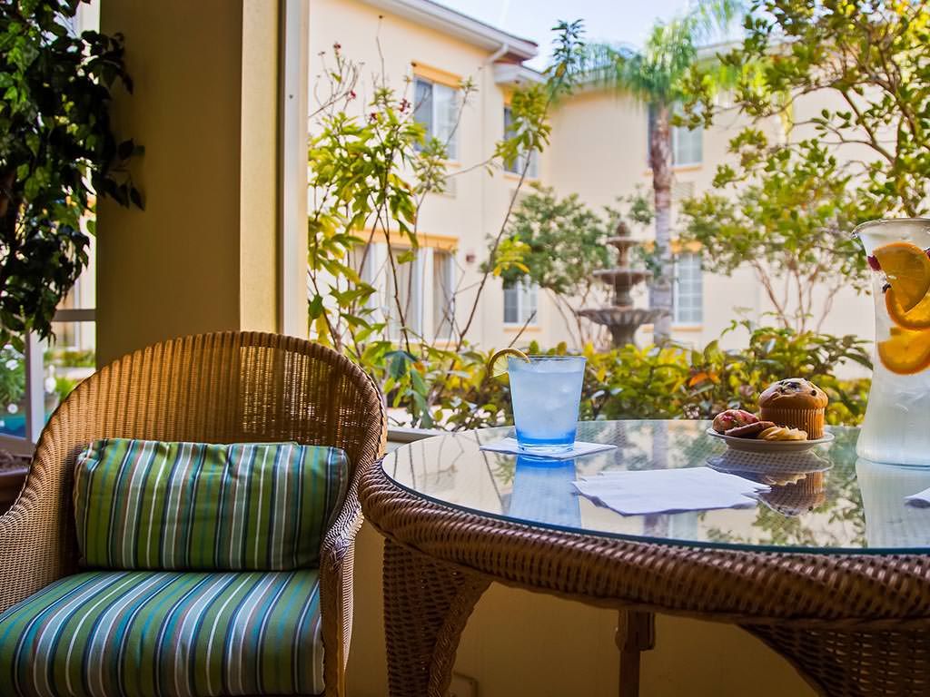 A cozy patio setting with a wicker chair and table overlooking a sunny courtyard.