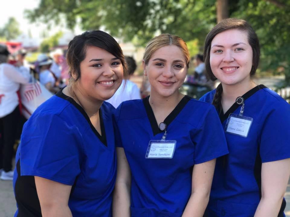 A group of people wearing blue scrubs smiling outdoors.