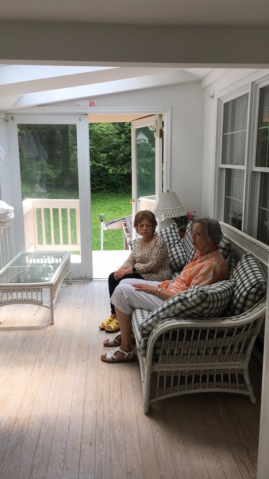 Two people sitting on a porch, engaged in conversation with a view of greenery outside.