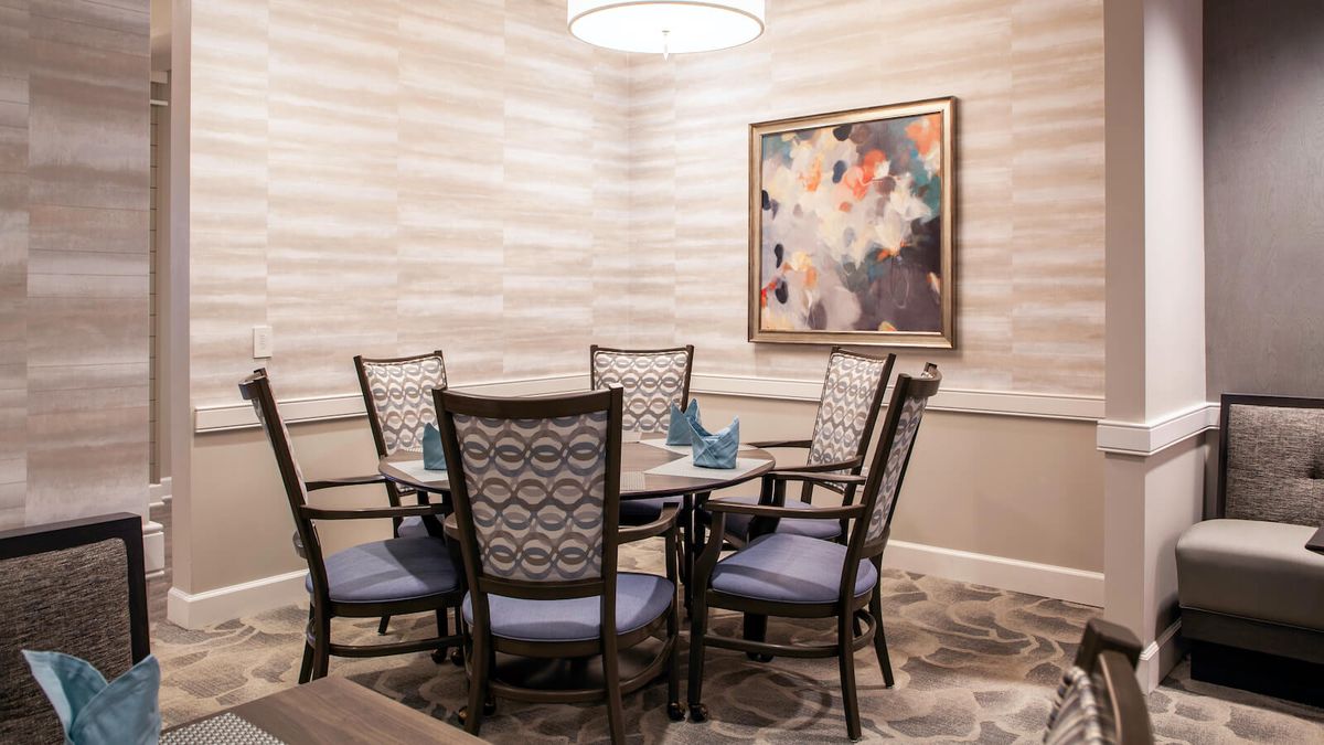 A modern dining room with a round table and elegant chairs, adorned by a colorful abstract painting on the wall.
