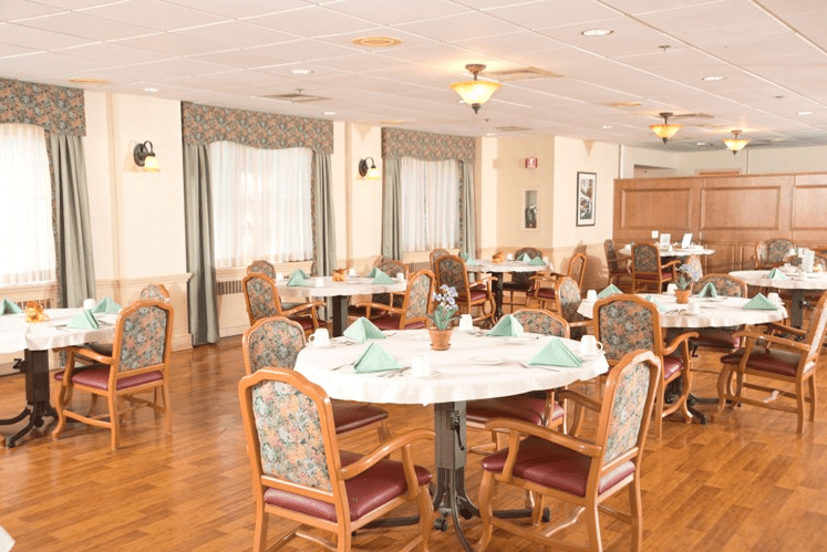 A well-arranged dining room with tables and chairs set up for guests, featuring decorative napkins and a cozy atmosphere.