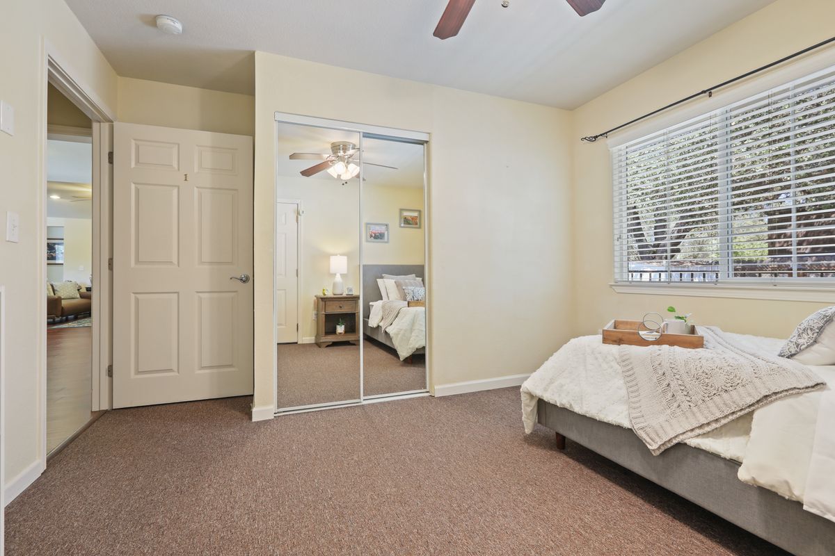 A cozy bedroom with a ceiling fan, mirror closet, and natural light.