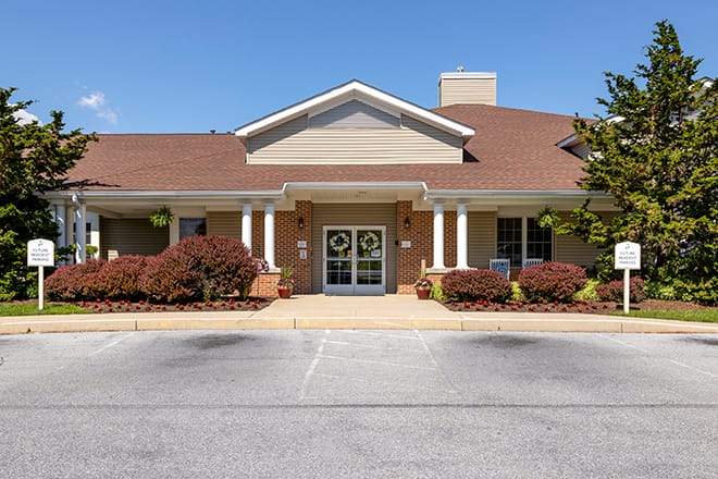 An exterior view of a brick building with a gabled roof and pillars at the entrance.
