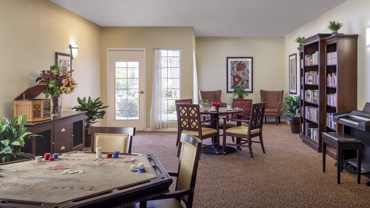 A cozy dining area with tables, chairs, and decorative plants next to large windows.