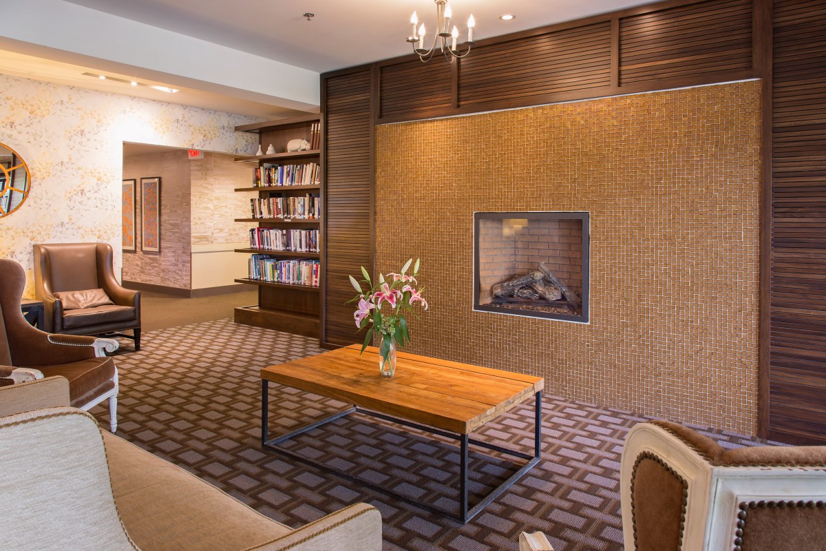 A cozy lounge area with a fireplace and a bookshelf, featuring a wooden table with a floral arrangement.