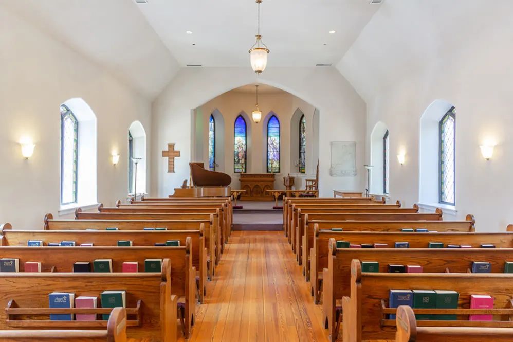Interior view of a church with wooden pews and stained glass windows.