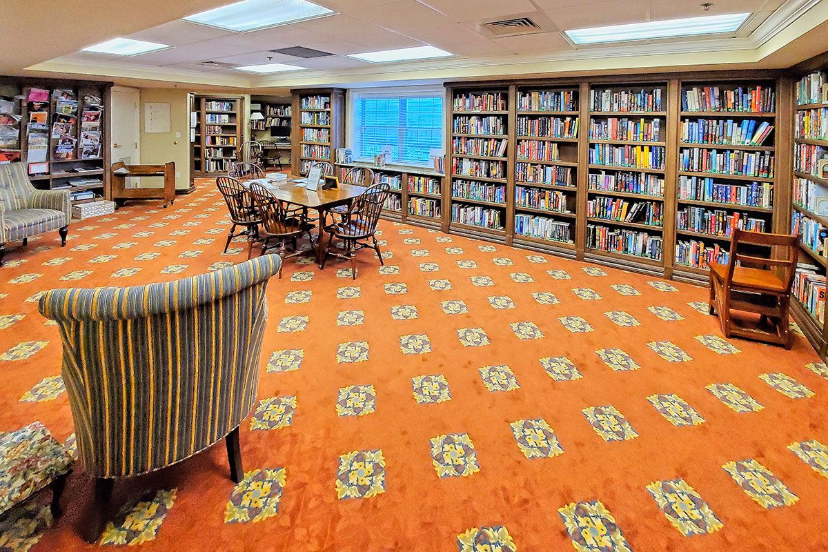 A cozy library with wooden bookshelves and an orange carpeted floor, featuring a central reading area.