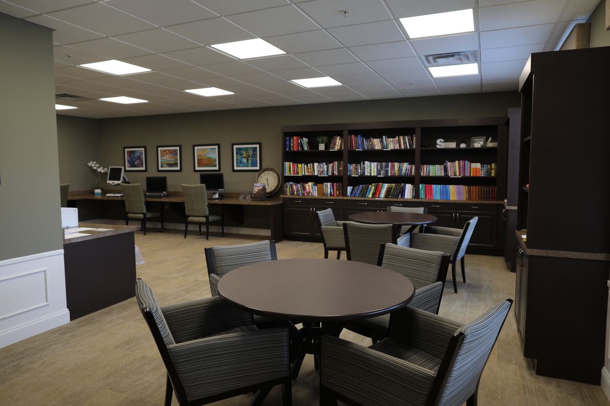 A quiet library room with round tables, comfortable chairs, bookshelves, and computers.