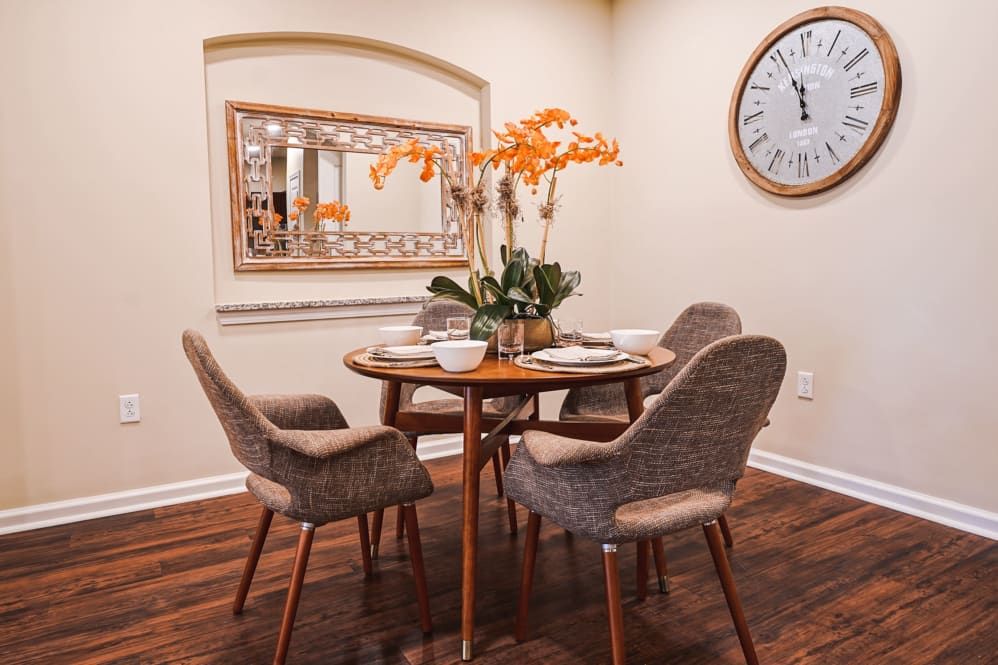 A cozy dining area with a wooden table and four cushioned chairs, adorned with vibrant orange flowers and surrounded by stylish decor.