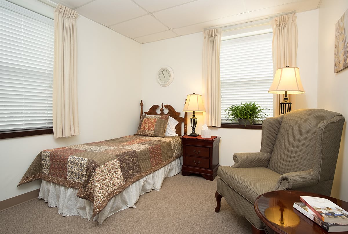 A cozy bedroom with a single bed, an armchair, and a nightstand by the window.