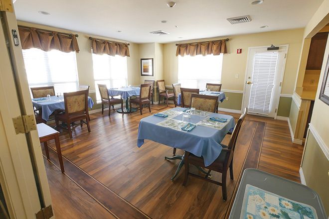 A neatly arranged dining area with several tables and chairs, featuring wooden floors and natural light from windows.