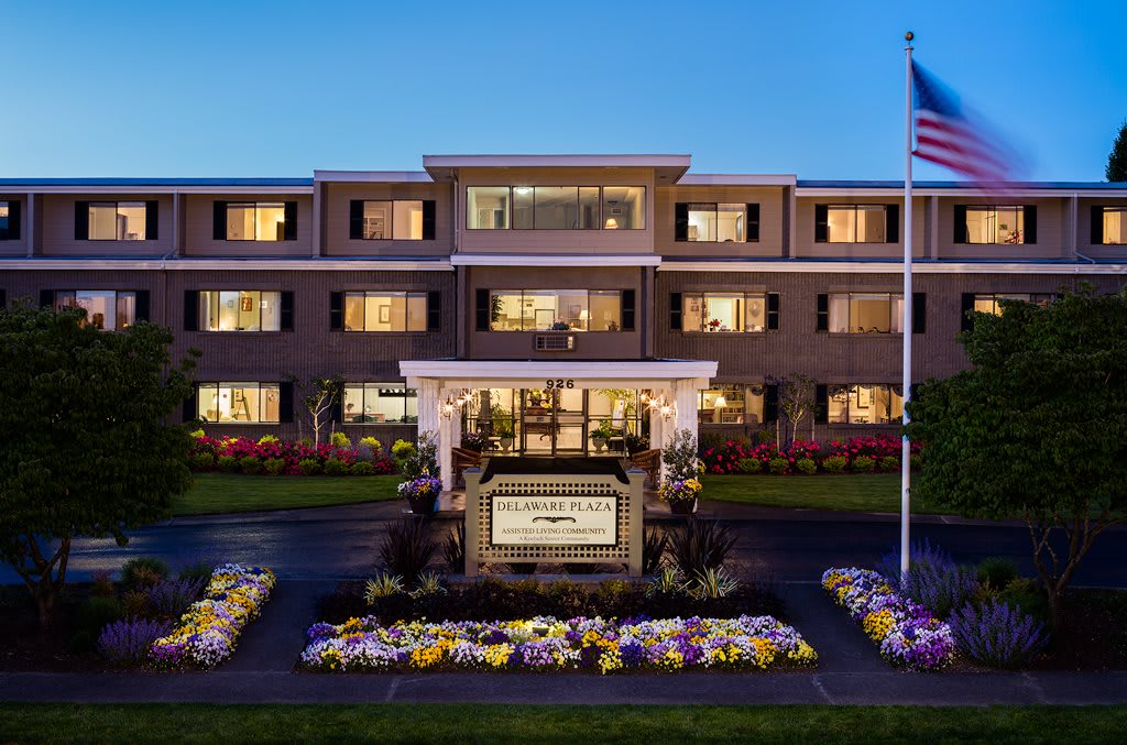 A well-lit hotel building at night with a flag and flower arrangements in the foreground.