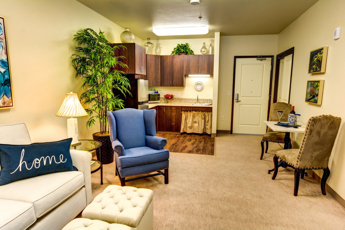 Cozy living room with a blue armchair, sofa, and kitchenette.