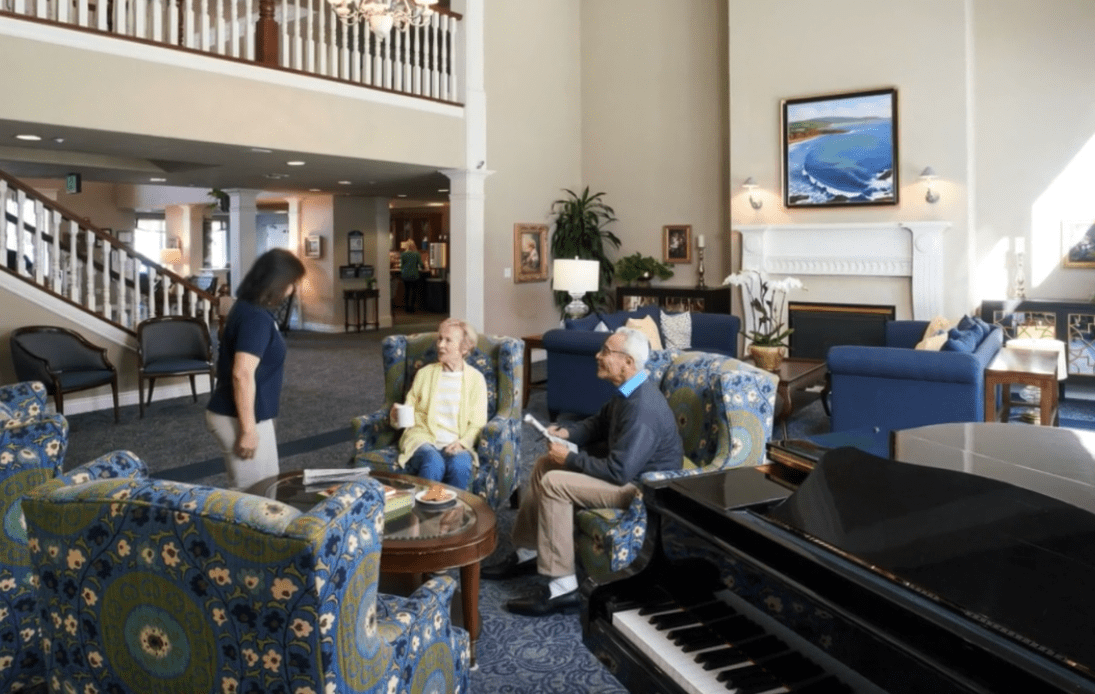 A spacious lobby with people engaging in conversation around a seating area, featuring a piano in the foreground.