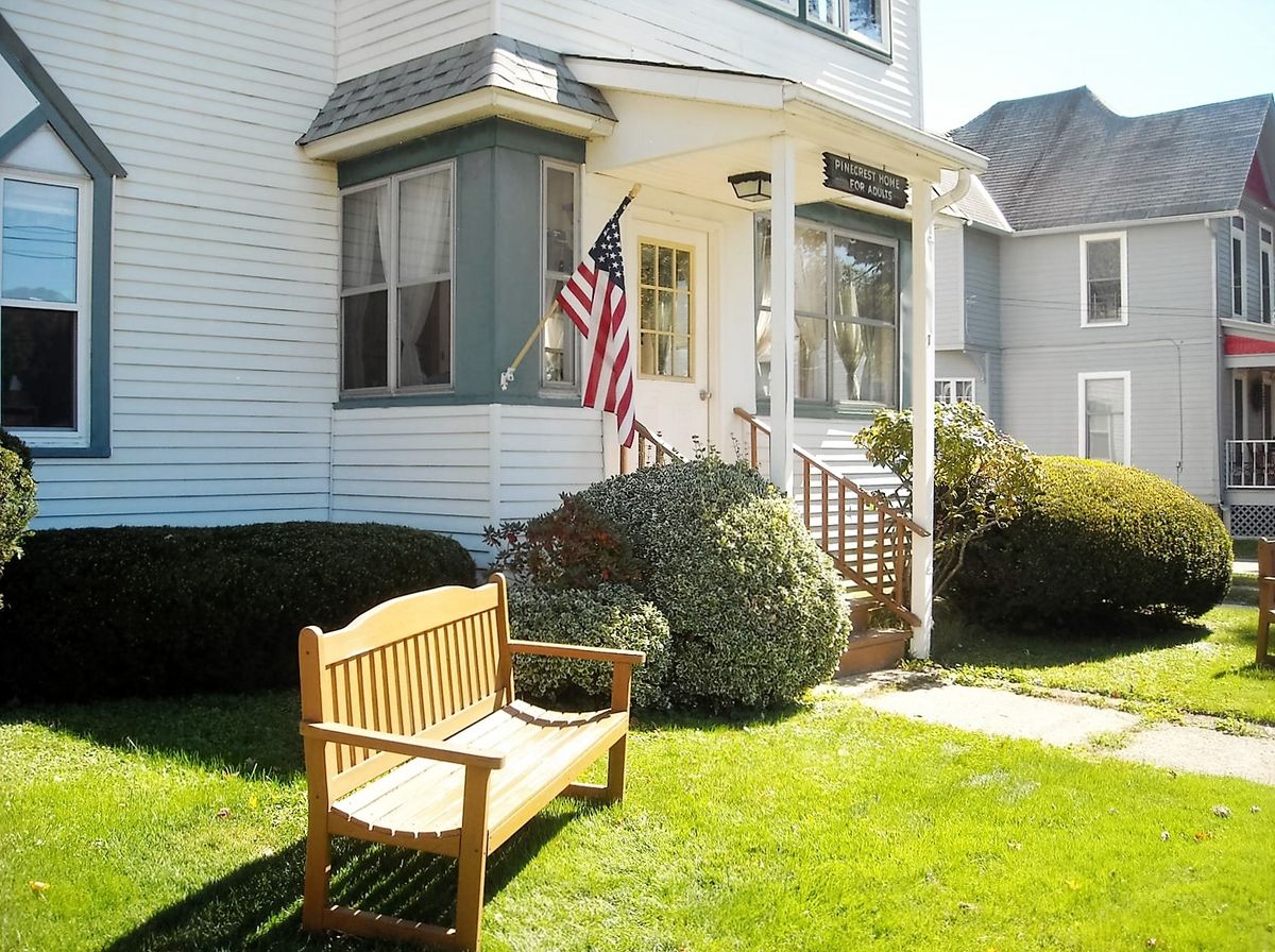 A quaint suburban house with an American flag displayed on the front porch and a wooden bench on the lawn.