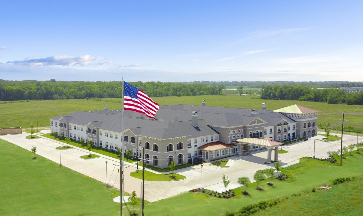 A large building with an American flag flying in front, surrounded by a parking lot and greenery.