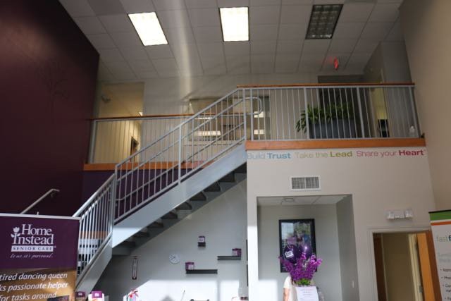 A modern office interior featuring a staircase and balcony with plants.