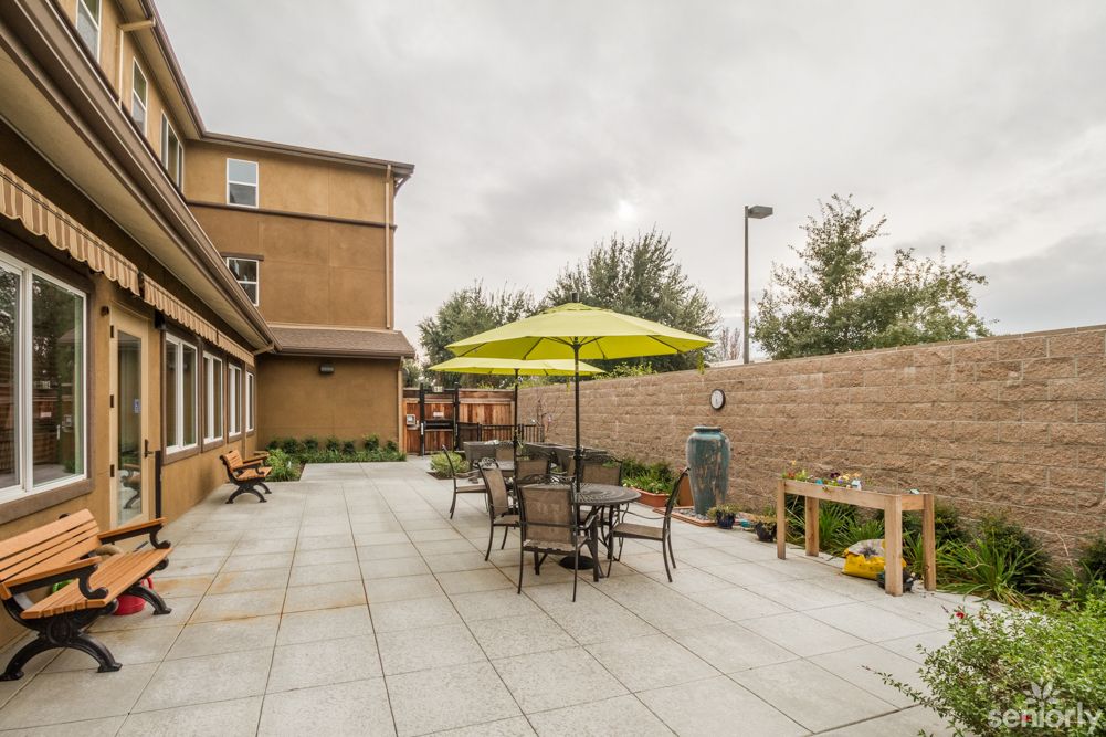 A patio area with tables, chairs, and an umbrella set against a brick wall.