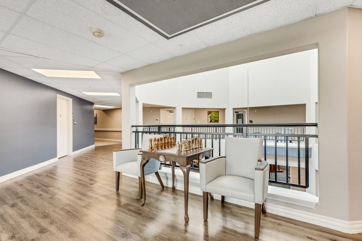 A spacious interior with a wooden floor, featuring two chairs and a small table next to a balcony railing.