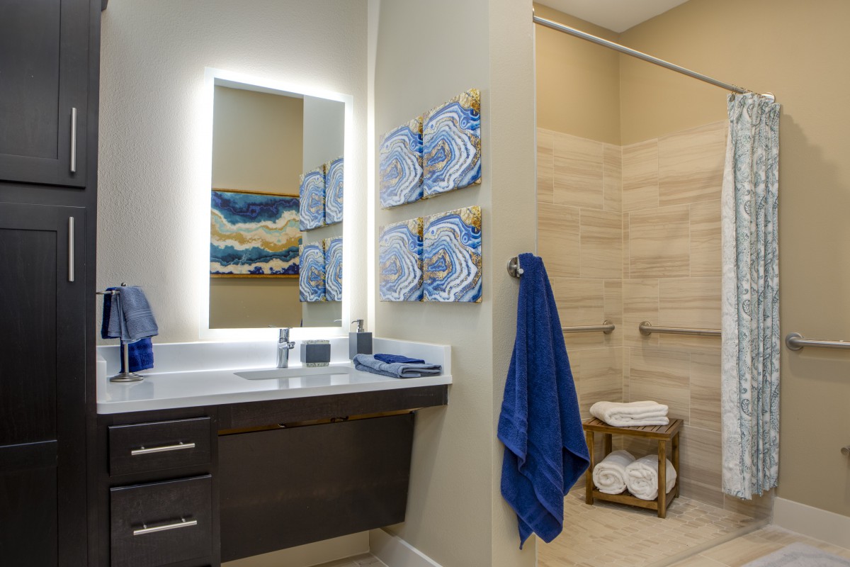 A modern bathroom with illuminated mirror, blue towels, and abstract artwork on the walls.