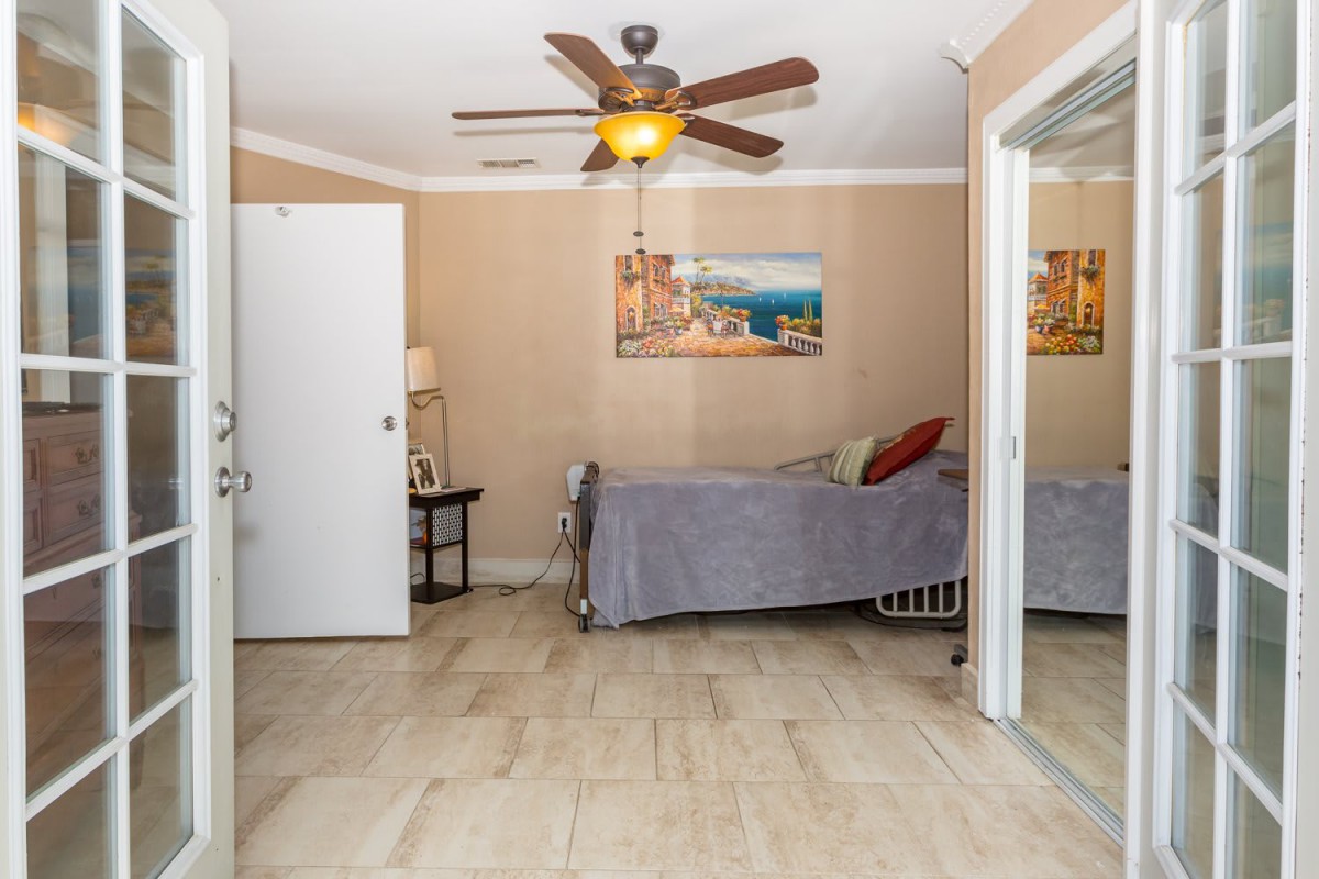 A cozy bedroom with a single bed, ceiling fan, and a painting on the wall.
