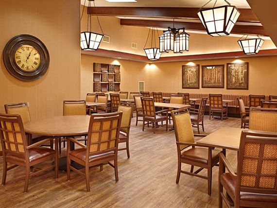 A cozy dining area with wooden tables and chairs, warmly lit by decorative light fixtures.