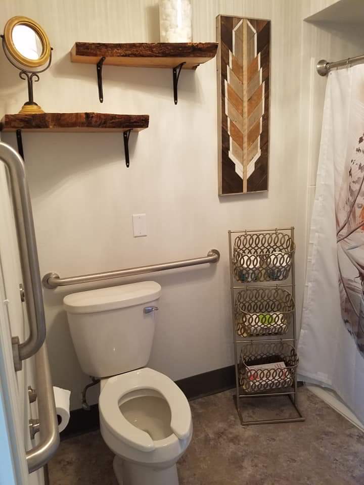 A compact bathroom with a toilet, shelves, a decorative shower curtain, and a towel rack.