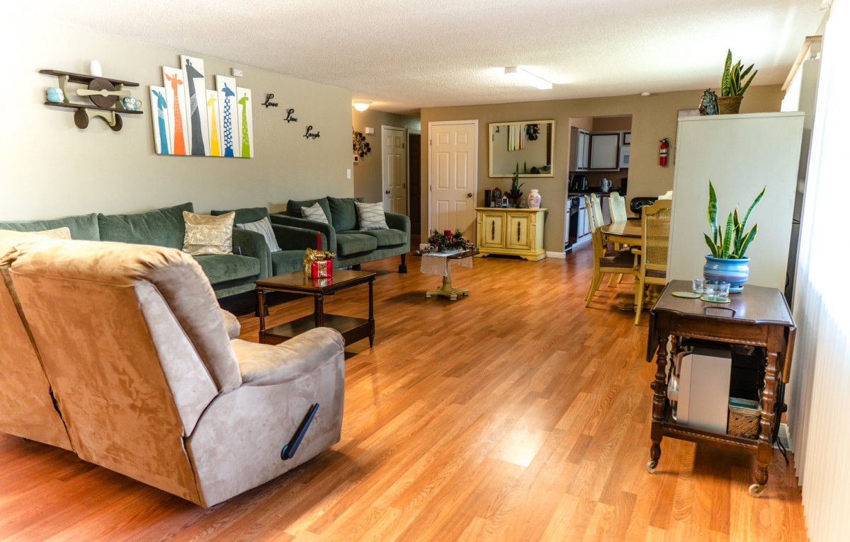 A spacious living room with wood flooring, featuring comfortable couches, a recliner, and modern wall art.