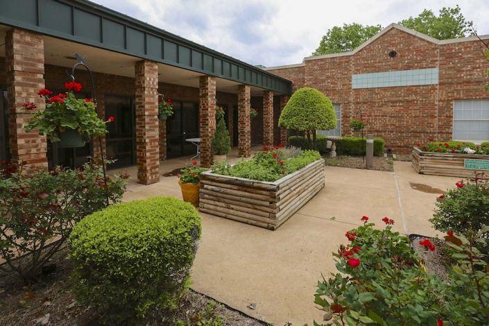 A serene courtyard with lush greenery and planter boxes surrounded by a brick building.
