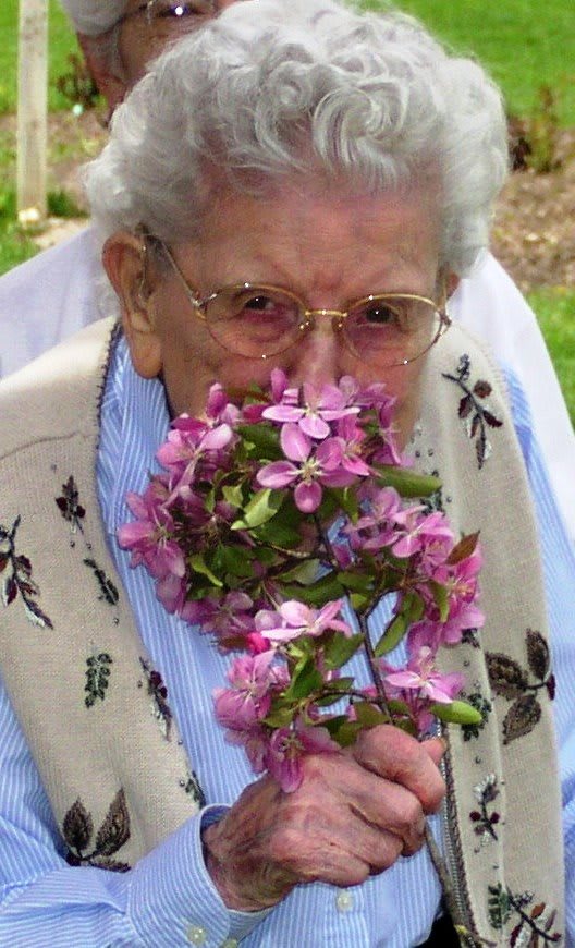 An elderly woman enjoying the scent of a vibrant bouquet of flowers outdoors.